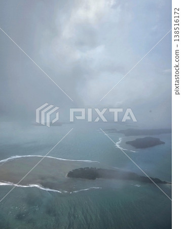 Dramatic overcast aerial shot looking down at dark landmasses and shallow turquoise reefs of the Andaman and Nicobar Islands scattered in the sea. 138516172