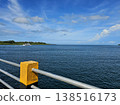 Scenic coastal view from a pier featuring yellow and black concrete bollards, looking out over calm ocean waters towards a distant green island. 138516173
