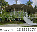 Exterior view of an elevated, modern eco-resort cottage with a curved roof and large windows, set amidst lush tropical gardens in the Andaman Islands. 138516175