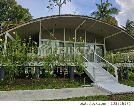 Exterior view of an elevated, modern eco-resort cottage with a curved roof and large windows, set amidst lush tropical gardens in the Andaman Islands. 138516175