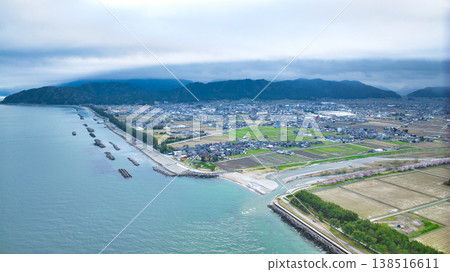 A view from the mouth of a small stream in eastern Toyama Prefecture in early spring, showing the Northern Alps and offshore wind turbines hidden by clouds. 138516611
