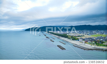 A view from the mouth of a small stream in eastern Toyama Prefecture in early spring, showing the Northern Alps and offshore wind turbines hidden by clouds. 138516632