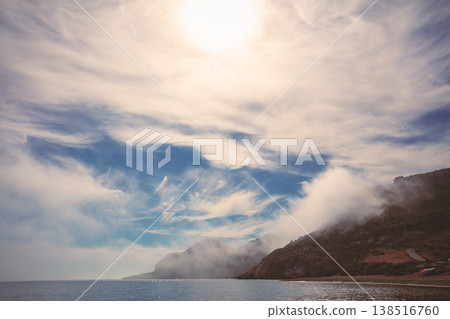 Seascape with a cloudy sky. Rocky bay with a calm sea. Clouds under the cliffs. Las Negras, Almeria, Spain. 138516760