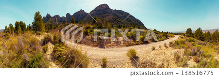 Panoramic view of mountain ridge and valley with dirt road on a sunny day. Road to Coves del Canelobre near Busot, Alicante, Spain 138516775