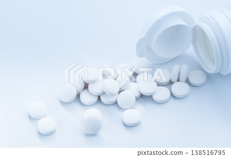Medicine pills capsule spilling out of bottle on blue background. White round pills. A heap of small round meds close up. Painkillers or prescription drugs consumption. 138516795