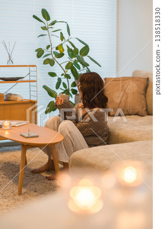An Asian woman relaxing in her living room at night, sipping a hot drink. An Asian woman relaxing in her living room at night, sipping a hot drink. 138518330
