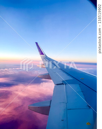 Airplane wing against a colorful sky at sunset. Soft clouds are visible below, creating a serene travel atmosphere. 138519902
