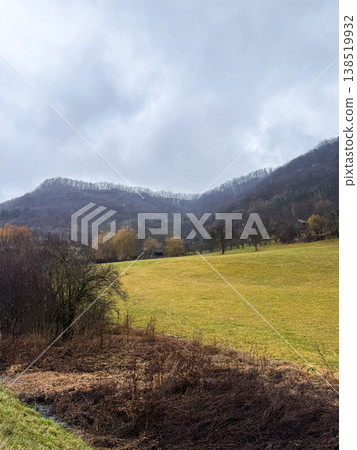 A scenic view of a rural landscape in Geislingen, Germany. A winding road leads through a grassy field under a cloudy sky, surrounded by hills. 138519932