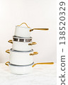 A vertical composition of four stacked ceramic pots in matte white finish, each with golden handles and matching lids. Photographed against a neutral background on a marble surface. Great for 138520329