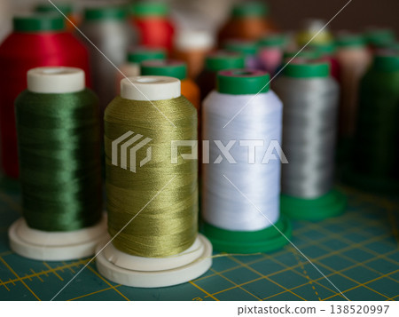 Colorful spools of sewing and embroidery thread arranged on a cutting mat. The vibrant threads showcase a variety of textures and hues for creative textile projects Colorful spools of sewing and embroidery thread arranged on a cutting mat. The vibrant threads showcase a variety of textures and hues for creative textile projects 138520997