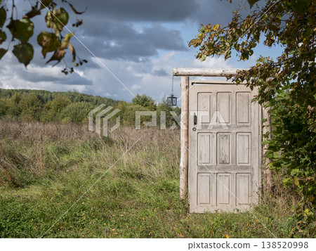 Freestanding weathered wooden door stands alone at the edge of an open field. The surreal scene evokes themes of escape, transition, and unexpected possibilities Freestanding weathered wooden door stands alone at the edge of an open field. The surreal scene evokes themes of escape, transition, and unexpected possibilities 138520998