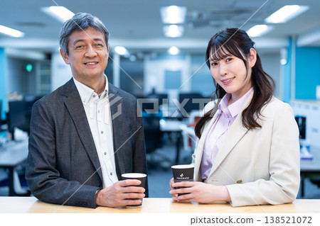 Office workers, a man and a woman, chatting while drinking coffee in the office. 138521072