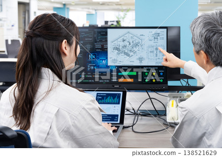 A man and a woman in work clothes are having a meeting while looking at a computer screen. 138521629