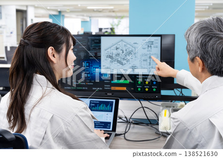 A man and a woman in work clothes are having a meeting while looking at a computer screen. 138521630