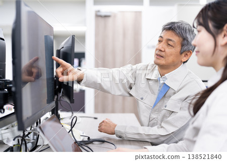 A man and a woman in work clothes are having a meeting while looking at a computer screen. A man and a woman in work clothes are having a meeting while looking at a computer screen. 138521840