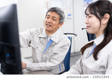 A man and a woman in work clothes are having a meeting while looking at a computer screen. A man and a woman in work clothes are having a meeting while looking at a computer screen. 138521843