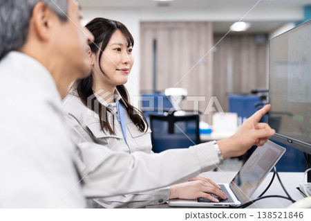 A man and a woman in work clothes are having a meeting while looking at a computer screen. A man and a woman in work clothes are having a meeting while looking at a computer screen. 138521846