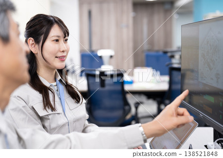 A man and a woman in work clothes are having a meeting while looking at a computer screen. 138521848