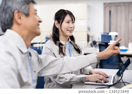 A man and a woman in work clothes are having a meeting while looking at a computer screen. 138521849