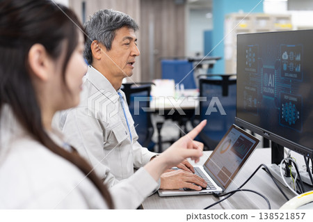 A man and a woman in work clothes are having a meeting while looking at a computer screen. A man and a woman in work clothes are having a meeting while looking at a computer screen. 138521857