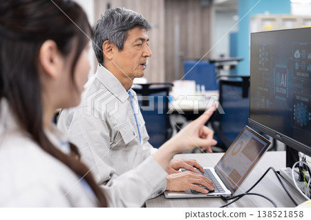 A man and a woman in work clothes are having a meeting while looking at a computer screen. A man and a woman in work clothes are having a meeting while looking at a computer screen. 138521858