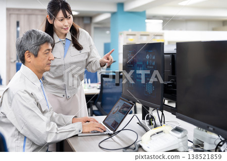 A man and a woman in work clothes are having a meeting while looking at a computer screen. 138521859