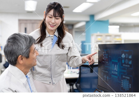 A man and a woman in work clothes are having a meeting while looking at a computer screen. A man and a woman in work clothes are having a meeting while looking at a computer screen. 138521864