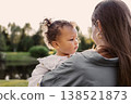 Mother Holding Toddler Daughter Outdoors at Sunset. Beautiful little child girl in arms of mom in green park 138521873
