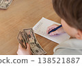 Child counting US dollar cash and writing finance notes on paper on beige wooden table. Early financial literacy, budgeting skills and money awareness concept with copy space indoors 138521887
