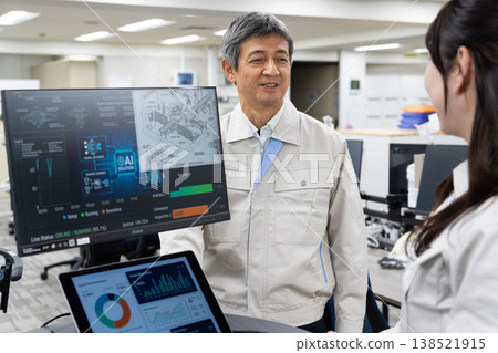 A man and a woman in work clothes are having a meeting while looking at a computer screen. 138521915