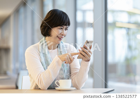 一位六十多歲的女士在咖啡桌旁使用智慧型手機。 一位六十多歲的女士在咖啡桌旁使用智慧型手機。 138522577