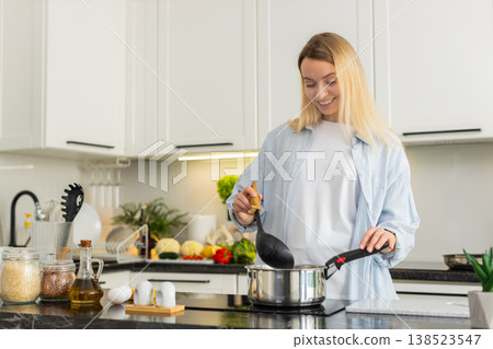Young woman slowly seasoning homemade soup in pot on electric cooktop for healthy lunch at home 138523547