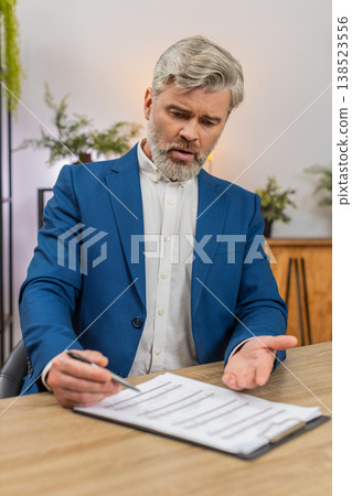 Middle-aged businessman spots invoice error fixes figures with pen then signs key papers confidently Middle-aged businessman spots invoice error fixes figures with pen then signs key papers confidently 138523556