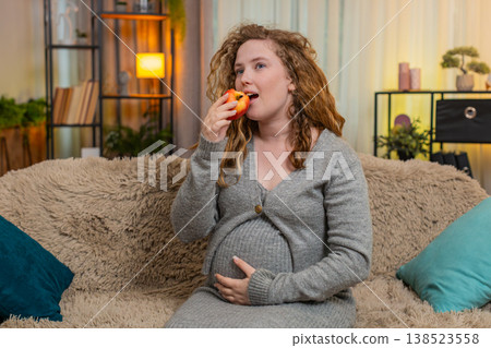 Pregnant woman eating apple, gently touching belly, relaxed with calm expression and healthy glow Pregnant woman eating apple, gently touching belly, relaxed with calm expression and healthy glow 138523558