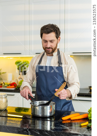 Middle-aged man seasoning homemade healthy soup on electric stove in home kitchen for hot diet meal Middle-aged man seasoning homemade healthy soup on electric stove in home kitchen for hot diet meal 138523575