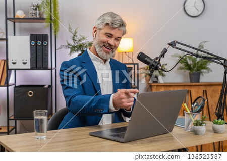 Middle-aged businessman records podcast on studio microphone gesturing actively sharing live ideas Middle-aged businessman records podcast on studio microphone gesturing actively sharing live ideas 138523587