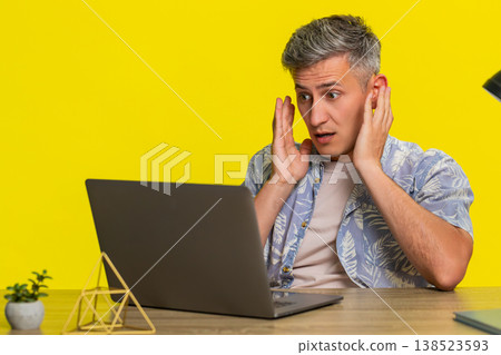 Man shocked by email on laptop reading message at table and leaning back reacting to surprise news 138523593