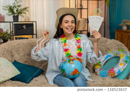 Happy woman on sofa with swim ring holding globe and plane tickets planning exciting future trip Happy woman on sofa with swim ring holding globe and plane tickets planning exciting future trip 138523637