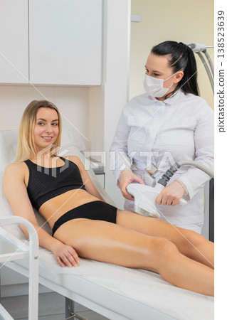 Young woman gets vacuum roller massage on legs with LPG device in beauty clinic for body sculpting Young woman gets vacuum roller massage on legs with LPG device in beauty clinic for body sculpting 138523639