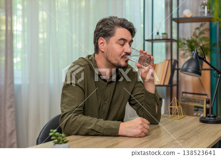 Middle-aged man drinks water glass practicing healthy habit hydration wellness routine at table desk 138523641