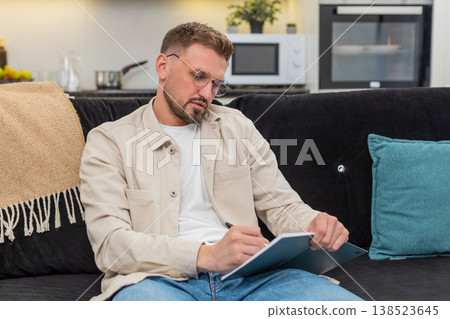 Young man drafts daily plan in notebook sets priorities makes schedule and maps tasks for week plans Young man drafts daily plan in notebook sets priorities makes schedule and maps tasks for week plans 138523645