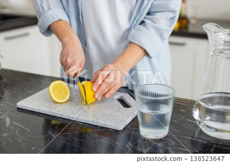 Hands slicing fresh lemon for water in home kitchen preparing healthy detox drink closeup shot 138523647