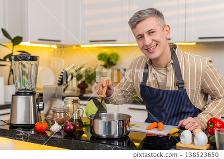 Middle-aged man preparing healthy diet soup in kitchen smiling during homemade meal routine at home Middle-aged man preparing healthy diet soup in kitchen smiling during homemade meal routine at home 138523650
