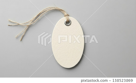 Blank oval tag with string hanging on a gray surface for labeling items or gifts Blank oval tag with string hanging on a gray surface for labeling items or gifts 138523869