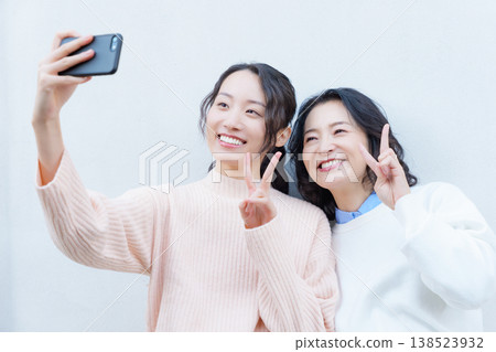 A portrait of a close mother and daughter taking a selfie on the veranda with their smartphones. A portrait of a close mother and daughter taking a selfie on the veranda with their smartphones. 138523932