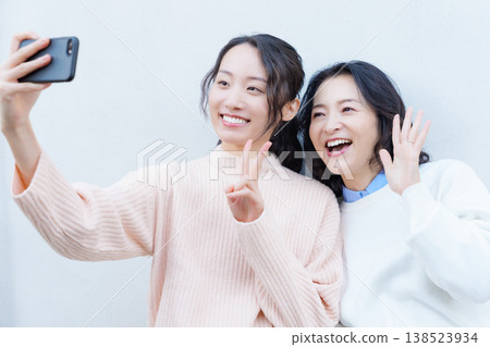 A portrait of a close mother and daughter taking a selfie on the veranda with their smartphones. A portrait of a close mother and daughter taking a selfie on the veranda with their smartphones. 138523934