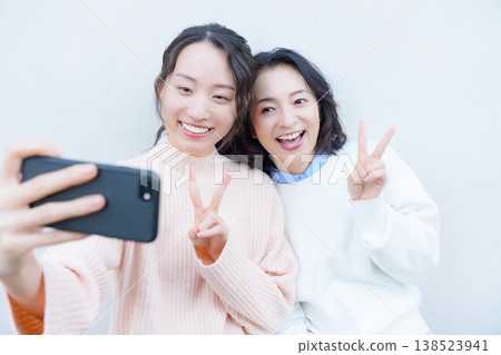 A portrait of a close mother and daughter taking a selfie on the veranda with their smartphones. A portrait of a close mother and daughter taking a selfie on the veranda with their smartphones. 138523941