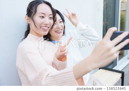 A portrait of a close mother and daughter taking a selfie on the veranda with their smartphones. A portrait of a close mother and daughter taking a selfie on the veranda with their smartphones. 138523945