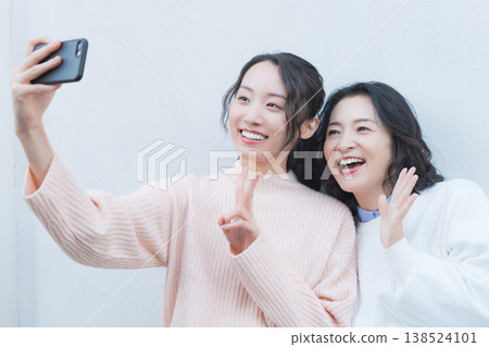 A portrait of a close mother and daughter taking a selfie with their smartphone on a retro-style veranda. A portrait of a close mother and daughter taking a selfie with their smartphone on a retro-style veranda. 138524101