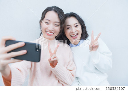A portrait of a close mother and daughter taking a selfie with their smartphone on a retro-style veranda. A portrait of a close mother and daughter taking a selfie with their smartphone on a retro-style veranda. 138524107